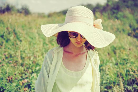 Attractive young woman in sunglasses and a hat resting in summer park. Image with instagram color effect