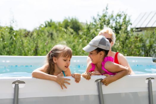 Mother and two daughters playing in pool water.Woman and two girls have fun in home pool splashing water and smiling