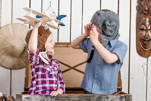 smiling little girl with wooden plane in hand and boy in pilot hat sitting in big chest