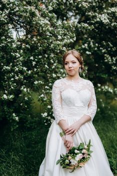 bride with a wedding bouquet in the forest near the bushes blooming with white flowers