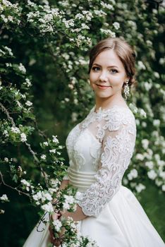 bride with a wedding bouquet in the forest near the bushes blooming with white flowers