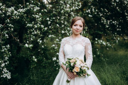 bride with a wedding bouquet in the forest near the bushes blooming with white flowers