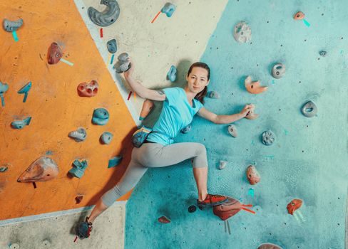 Sporty young woman standing on artificial boulders in climbing gym, looking at camera