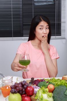 unhappy young woman drinking vegetable juice in kitchen