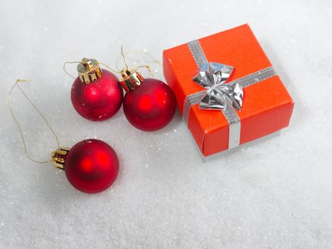 Red Christmas balls and gift box on a blue background in the snow, top view