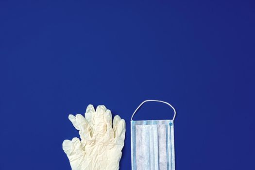 Medical gloves and surgical protective face mask on dark blue background. Coronavirus concept