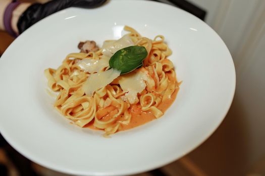 Waiter holding plate of tasty food. Italian cuisine in restaurant, pasta with cheese.