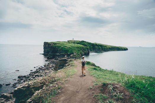 Traveler young woman with backpack walking on island in the sea in summer, rear view