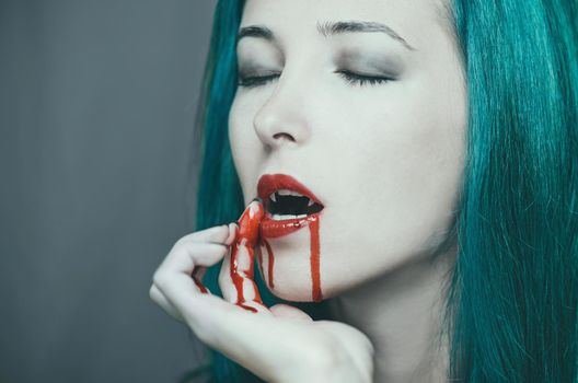 Beautiful vampire young woman wipes the blood from her lips. Halloween or horror theme