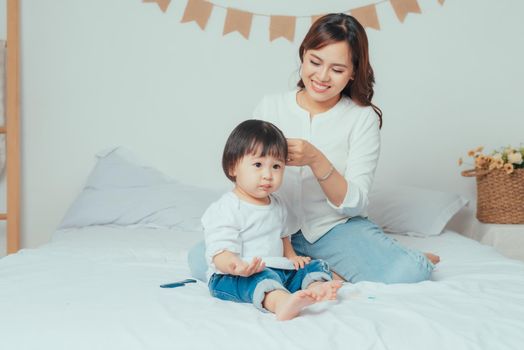 Beautiful young mother is combing her cute little daughter hair