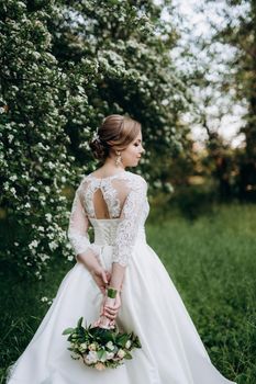 bride with a wedding bouquet in the forest near the bushes blooming with white flowers