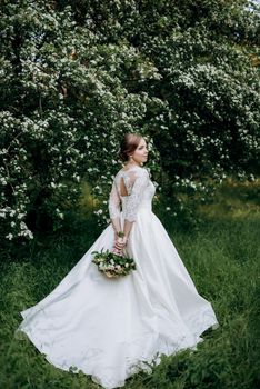 bride with a wedding bouquet in the forest near the bushes blooming with white flowers