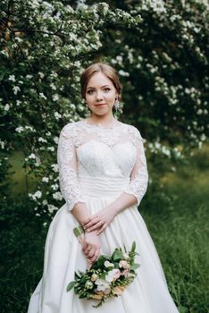 bride with a wedding bouquet in the forest near the bushes blooming with white flowers