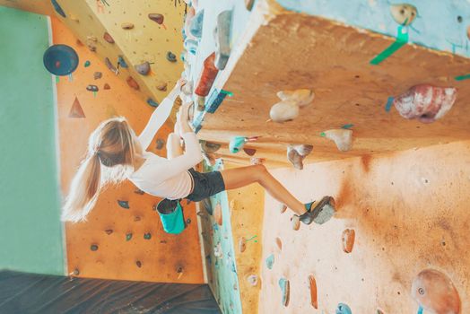 Free climber little girl practicing on artificial boulders in gym, bouldering