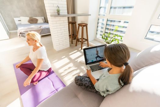 Young adult mother with her daughter watching online training together at home, looking a laptop