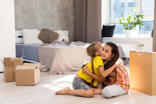 Happy family in living room. Preschool daughters sitting and help unpacking cardboard boxes belongings. Buy real estate, relocation at new modern house