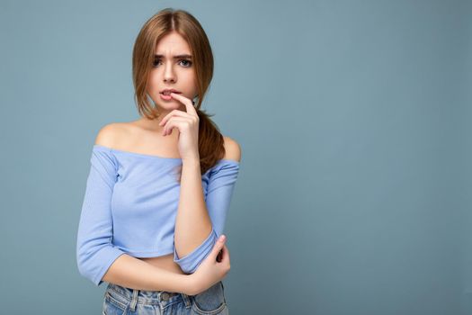Photo portrait of thoughtful young nice beautiful blonde woman with sincere emotions wearing trendy blue crop top isolated over background with empty space and thinking.