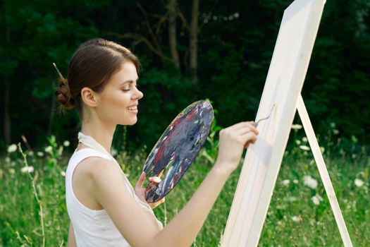 Woman in white dress with palette of paints on nature art drawing. High quality photo