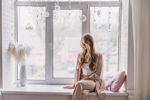 Resting and thinking woman in pajamas sitting on the window-sill at home. Side view