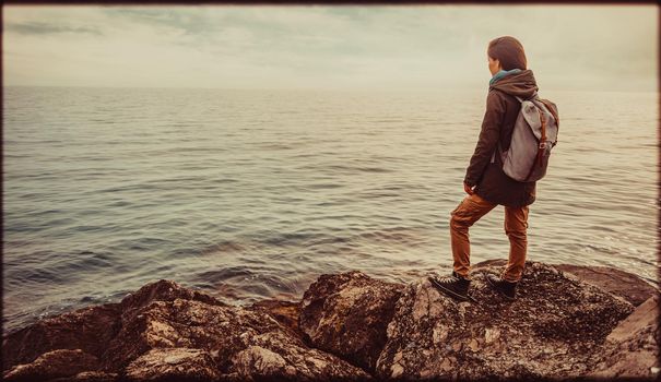 Traveler girl standing on stone coast and enjoying view of sea. Image with vintage color effect and rectangular frame