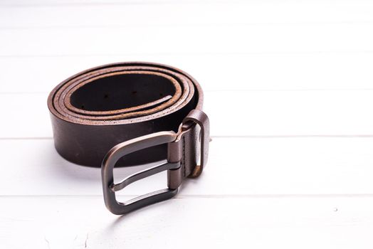 twisted brown male leather belt on wooden background, top view