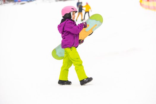 Snowboard Winter Sport. little girl learning to snowboard, wearing warm winter clothes. Winter background.