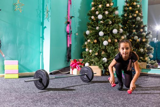 Merry Christmas and a happy new year. Little girl workout at home in christmas interior. Little dark-haired female model has exercises