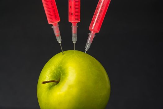 Red liquid in the syringe injected into apple on a black background, close-up