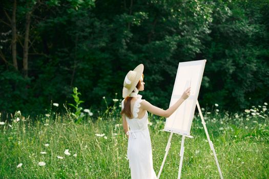 Woman in white dress in nature paints a picture of a landscape hobby. High quality photo