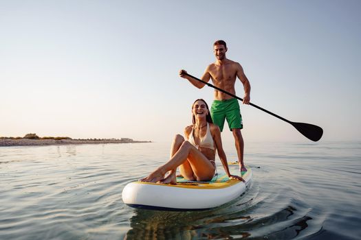 Couple of tourists young man and woman having fun paddleboarding at sea at sunset