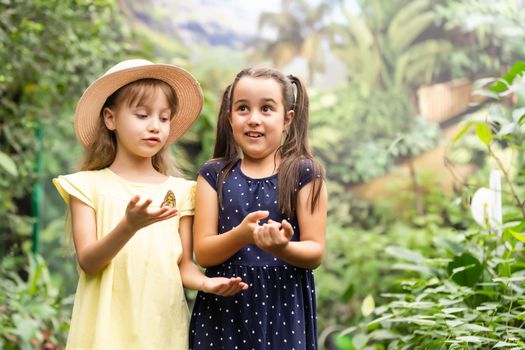 two little girls with butterflies in a greenhouse