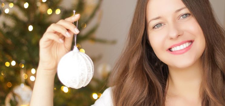 Decorating Christmas tree and winter holidays concept. Happy smiling woman holding festive ornament at home.