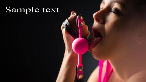 BDSM outfit for adult sex games. A young woman licks pink gag ball - image