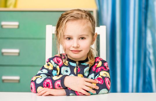 Happy liitle girl sitting at the table in her room and smiling