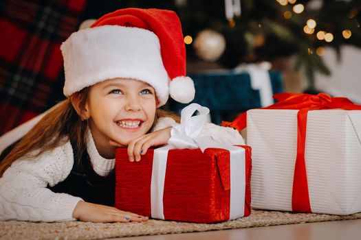 A happy little girl in a Santa Claus hat smiles with gifts in her hands.