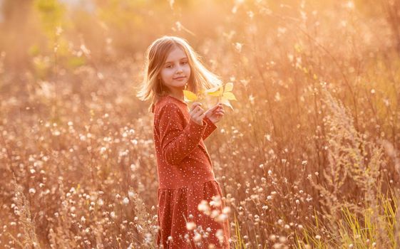 Smiling little girl with yellow autumn leaves on sunny nature background