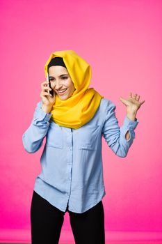 muslim woman in yellow hijab talking on the phone technology pink background. High quality photo