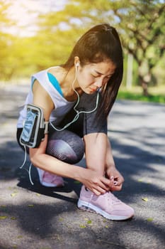 young sporty woman tying shoelaces while listening to music with earphones from her smartphone in the park 