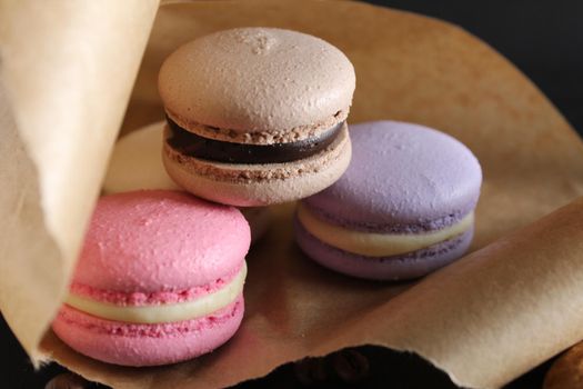 Three multi-colored macaroons on crafted brown paper next to lie sticks cinnamon on a black background with place for text and with a copyspace.