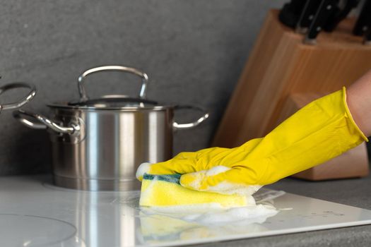 Female hands in yellow gloves cleaning electrical stove with a sponge close up