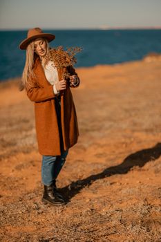 A woman walking along the coast near the sea. An elegant lady in a brown coat and a hat with fashionable makeup walks on the seashore.