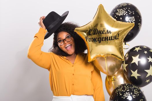 Portrait of smiling young African-American adult woman looking sweet on yellow background holding balloons.
