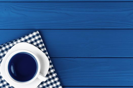 Top view of a cup of coffee on saucer on classic blue background. Close up.
