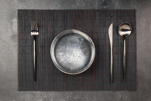 Empty black clay plate and sblack metal silverware set on wooden table