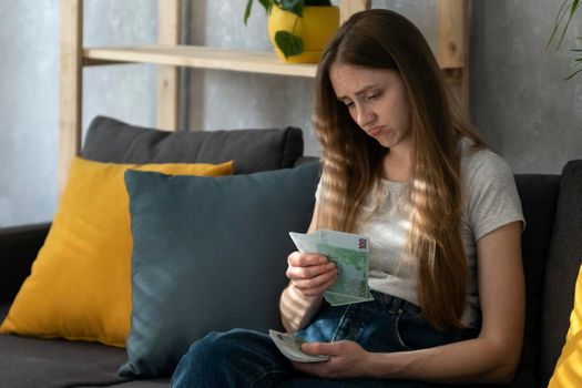 Young woman is counting money and is saddened by expenses Low salary. Inflation. Girl recounts her salary.