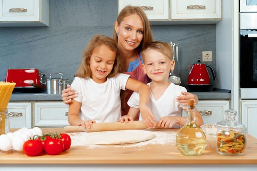 Mother and her little kids, boy and girl, helping her to prepare dough close up