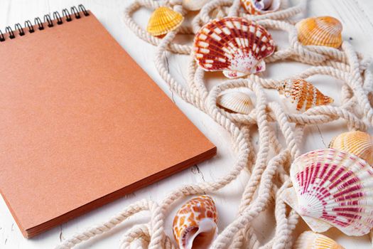 Close up photo of brown notepad with sea shells on wooden planks closeup, copy space
