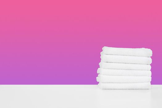 Stacked clean towels on white table against color background, front view