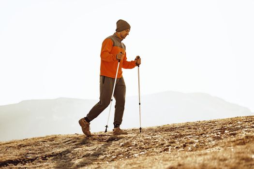 Man traveler in sportswear with trekking sticks going up the mountain