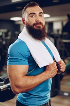 Positive bearded young man bodybuilder in blue t-shirt standing in gym